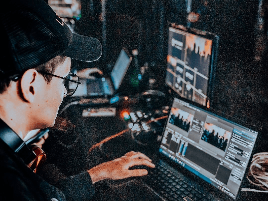 Person working on video editing at a computer with multiple screens displaying software interfaces.